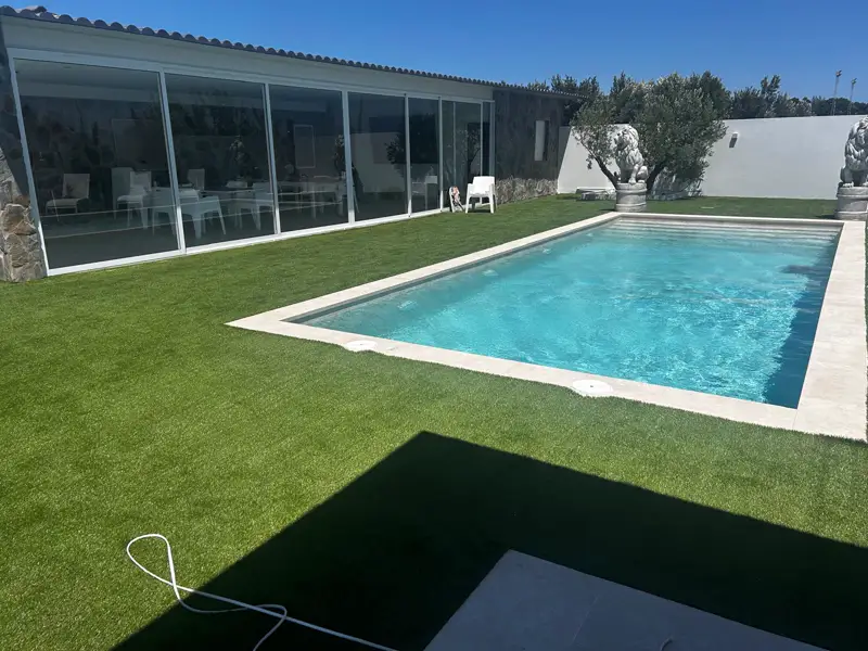 Pradera de césped artificial entre la piscina y el pabellón acristalado en Carrizal