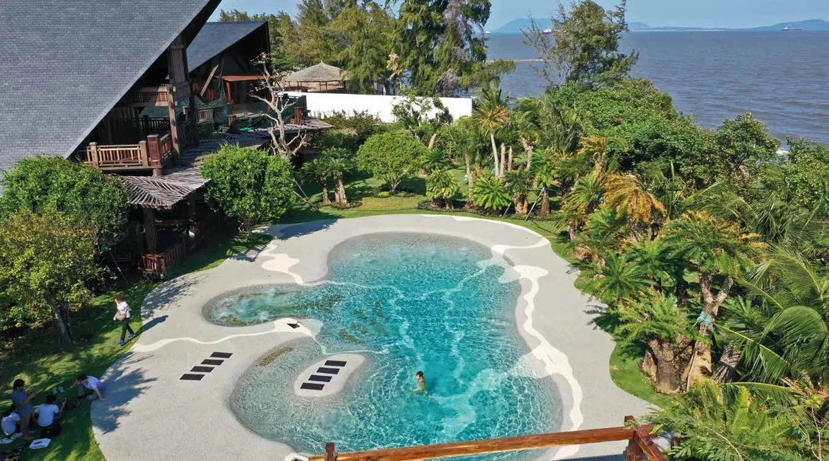 Piscina de arena Bio.design con entrada de playa y formas orgánicas en un jardín tropical