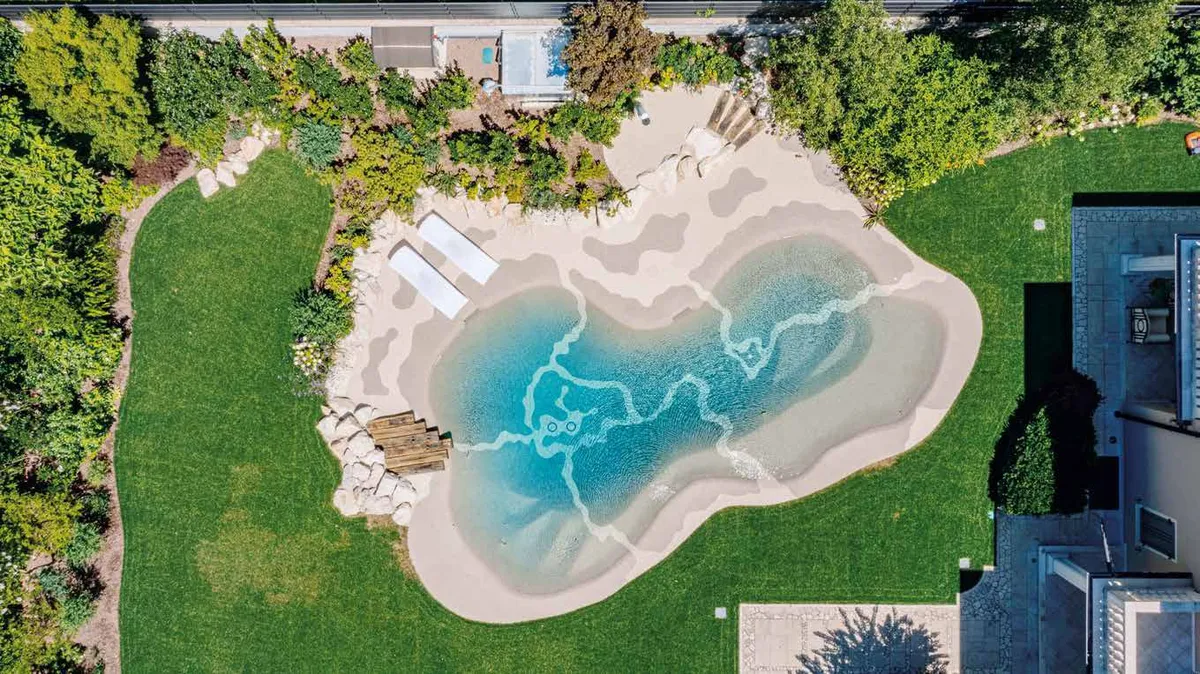 Vista aérea de una piscina de arena Bio.design de formas orgánicas rodeada de césped