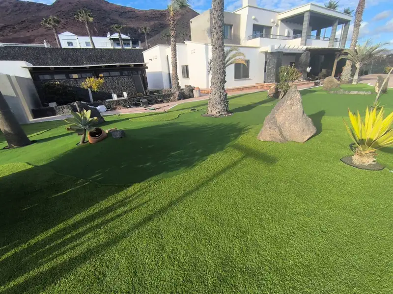 Jardines exteriores de un hotel en Meloneras con césped artificial, palmeras y rocas volcánicas
