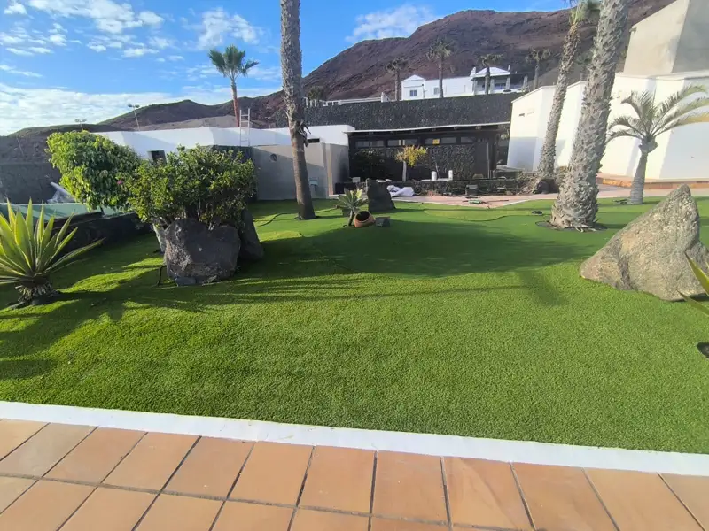 Césped artificial con palmeras y rocas volcánicas en un paseo marítimo de Lanzarote